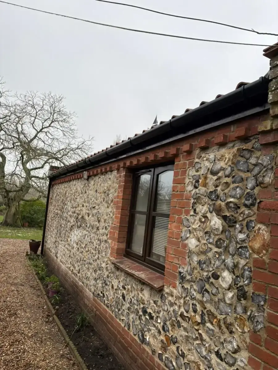 Deep-flow black uPVC guttering installed on a traditional Norfolk flint and brick cottage extension by Norfolk Exterior Solutions